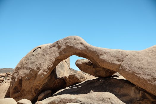 Natural rock arch formation in the arid landscape of Joshua Tree National Park under a clear blue sky.