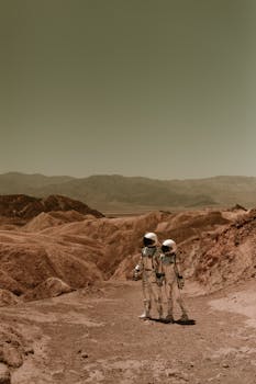 Two astronauts in spacesuits exploring a desolate, Mars-like desert landscape.